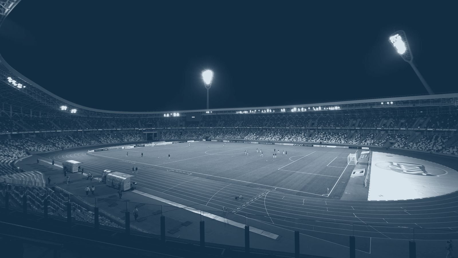 A floodlit stadium bowl at night, seen from the upper tier